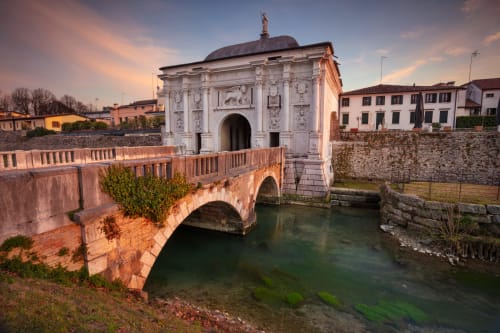 Storica porta veneziana e ponte sul canale a Treviso, Italia, al tramonto con architettura rinascimentale