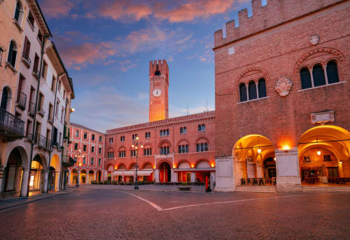Piazza dei Signori a Treviso al tramonto, con edifici medievali illuminati e torre storica in Italia