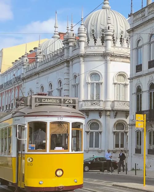 Elétrico amarelo 24 na rua Camões em Lisboa com edifício histórico branco e arquitetura com cúpula