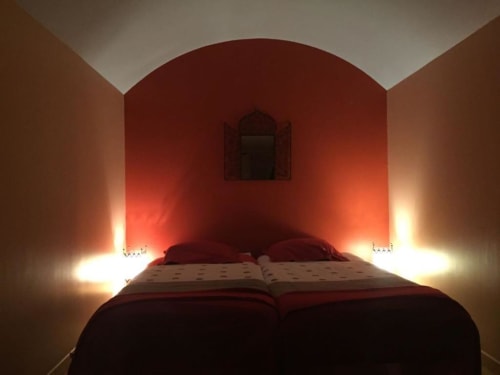 Chambre cosy à La Maison de Marie-Claire avec mur accentué rouge, éclairage ambiant et lit vue jardin