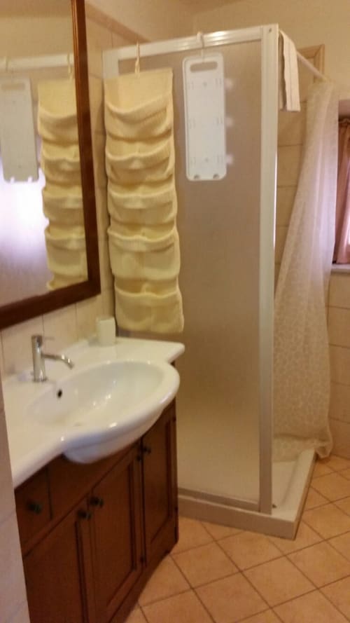 Modern bathroom in Il Casale di Nanni with white sink, shower enclosure, yellow storage organizer, and terra cotta tiles