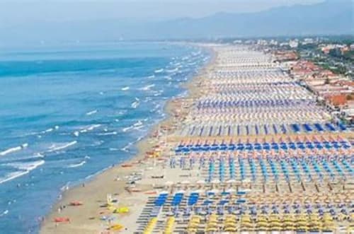 Aerial view of sandy beach with colorful umbrellas and loungers along Tuscany coastline near Lucca