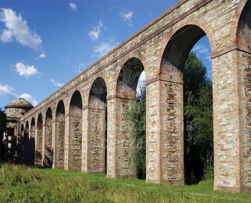 Historic arched aqueduct ruins in Lucca, Italy with ivy-covered pillars and blue sky