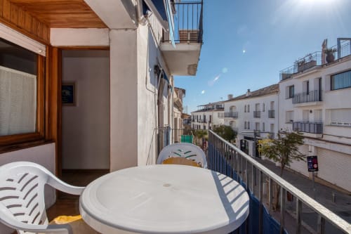 Sunny apartment balcony in Palafrugell with white table, chairs, and city views of neighboring buildings