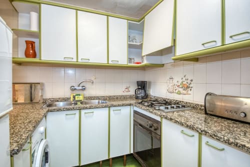 Modern kitchen with white and green cabinetry, granite countertops, and stainless steel appliances in Calella apartment