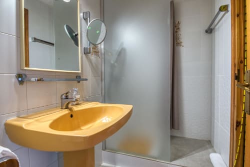 Modern bathroom with yellow pedestal sink, large mirror, glass shower enclosure, and white tile walls at Finques Garcia
