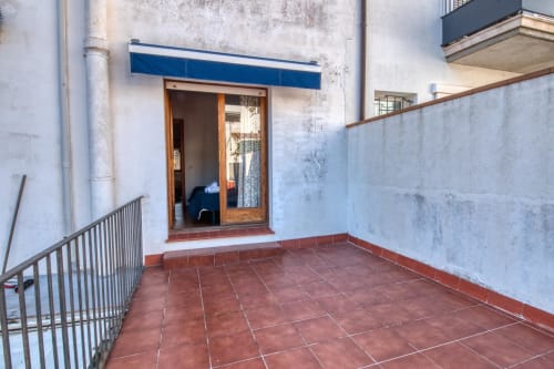 Terrace of a studio apartment in Calella de Palafrugell with red tile flooring, blue awning, wooden door, and city views
