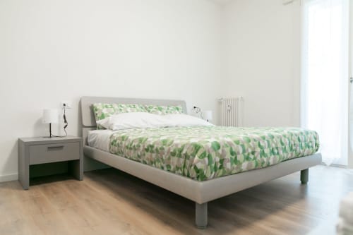 Modern bedroom with green leaf patterned bedding, gray nightstand, and bright natural light at Ca' Martha apartment in