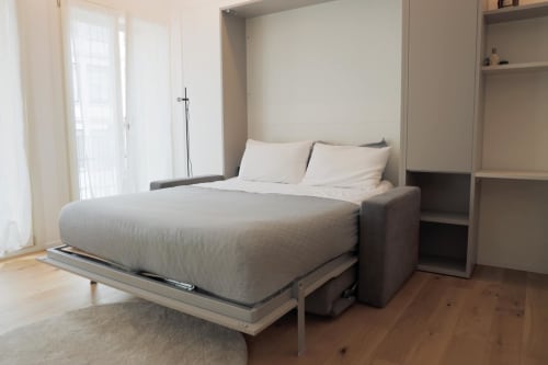 Letto a scomparsa moderno nell'appartamento di Treviso con biancheria grigia, armadi a muro, pavimenti in legno e accesso al balcone