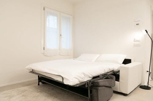 Divano letto moderno con biancheria bianca nell'appartamento minimalista Ca Borsa III a Treviso, con finestre sulla città e stile contemporaneo
