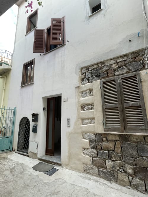 Exterior courtyard entrance of Casa Arborea apartment in Orosei, Italy with white walls and stone accents