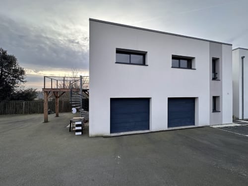 Immeuble moderne blanc avec deux portes de garage bleu foncé à L'Écrin du Blanc Caillou, Saint Pair sur Mer