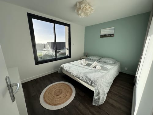 Chambre moderne à L'Écrin du Blanc Caillou avec vue mer, lit queen, mur vert menthe, parquet foncé et tapis rond