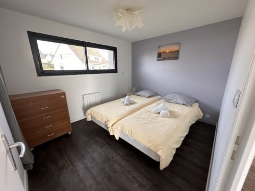 Lits jumeaux avec linge de lit crème dans une chambre moderne de L'Écrin du Blanc Caillou, Saint Pair sur Mer, sol foncé et vue mer
