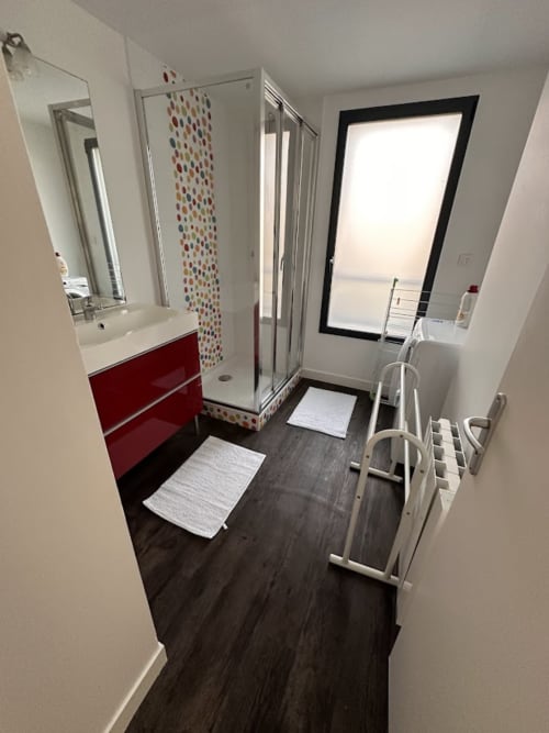 Salle de bain moderne avec vanité rouge, carrelage coloré, douche accessible et vue sur mer à l'appartement de Saint Pair sur Mer