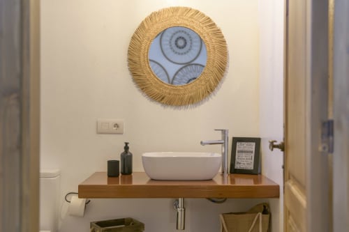 Modern bathroom sink with white ceramic bowl on wooden counter, gold framed mirror, and amenities at Finca de La Geria