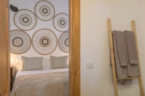 Bedroom in La Cochera cottage with decorative woven wall plates, bed with pillows, and wooden towel rack with gray towels