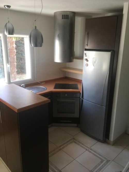 Cuisine moderne de l'appartement Nano House à Bègles avec appareils en acier inoxydable, luminaires suspendus et vue sur jardin