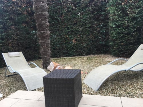 Terrasse de jardin de la Nano House à Bègles avec chaises longues, table d'appoint noire et haies de lierre