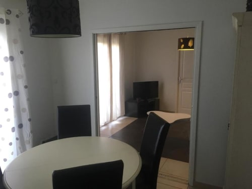 Coin repas du studio Nano House à Bègles : table ronde blanche, chaises noires et vue sur la chambre via miroir
