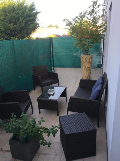 Terrasse jardin de la Nano House avec mobilier en rotin noir, plantes en pots et clôture de confidentialité verte à Bègles