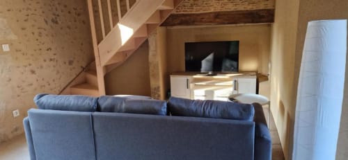 Canapé bleu dans le salon du gîte Escapade avec téléviseur, escalier en bois et vue sur le jardin au Domaine de la Grande Décision