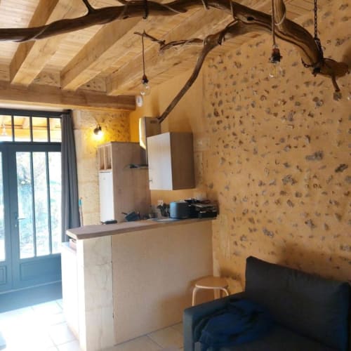 Rustic cottage interior with exposed wooden beams, stone walls, kitchenette, and lounge area at Domaine de la Grande Décision