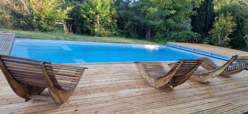 Wooden sun loungers on a terrace beside a blue swimming pool surrounded by trees at Domaine de la Grande Décision