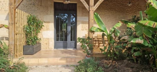 Entrée rustique en pierre avec poutres apparentes, portes sombres, terrasse et jardin au Domaine de la Grande Décision, La Douze