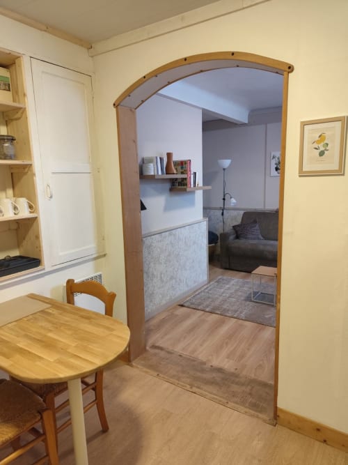 Appartement Accolade à Châteaudun avec table à manger en bois, porte voûtée vers le séjour et étagères de cuisine.