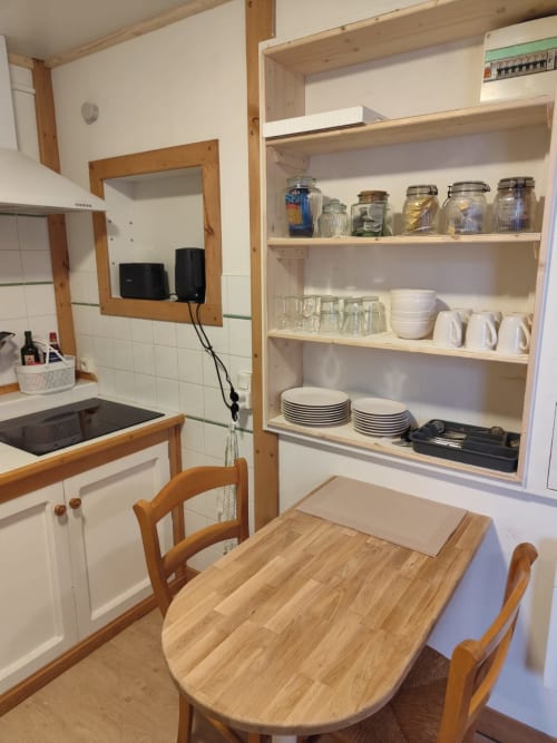 Cuisine avec table à manger, chaises en bois, étagères blanches avec vaisselle et provisions à l'appartement Accolade à Châteaudun