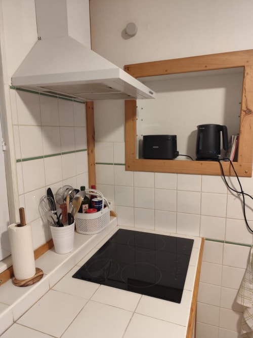 Coin cuisine moderne de l'appartement Accolade à Châteaudun, avec plaque de cuisson induction noire, hotte blanche, placards en bois, et