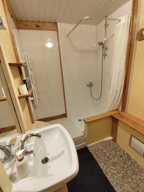Salle de bain moderne de l'appartement Accolade à Châteaudun avec douche blanche, lavabo et accents bois