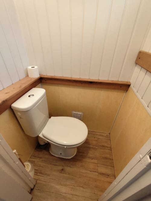 Salle de bain compacte de l'appartement Accolade à Châteaudun avec toilettes blanches, sol en bois et panneaux muraux beige clair