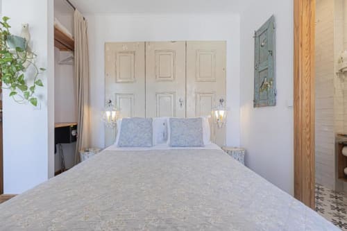 Premium bedroom at Ninho Saloio with queen bed, blue pillows, cream wardrobe, wall sconces, and wooden bathroom door