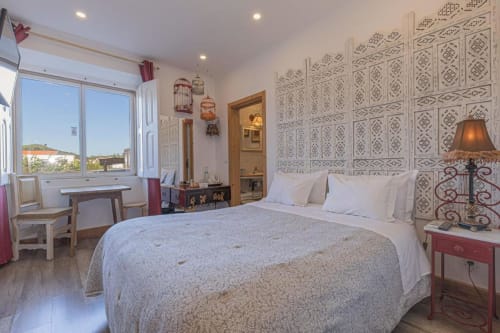 Bright bedroom at Ninho Saloio with queen bed, patterned headboard, and window overlooking Venda do Pinheiro countryside