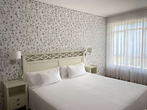 Luminosa habitación del Hotel Playa de Los Locos con ropa de cama blanca, papel tapiz con motivos de hojas y vistas al jardín en Suances