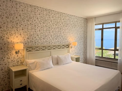 Habitación luminosa del Hotel Playa de Los Locos con vista costera, ropa de cama crema, papel pintado estampado e iluminación cálida
