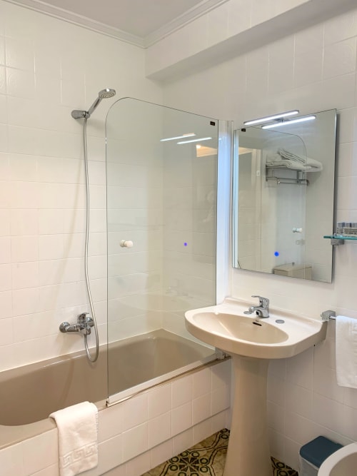 Baño moderno del Hotel Playa de Los Locos en Suances con ducha de cristal, lavamanos de pedestal y espejo iluminado