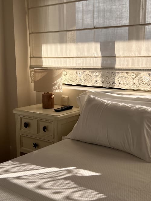 Habitación luminosa en Hotel Playa de Los Locos, Suances, con vistas al mar, ropa de cama blanca, mesita de noche y detalles de encaje en ventanas