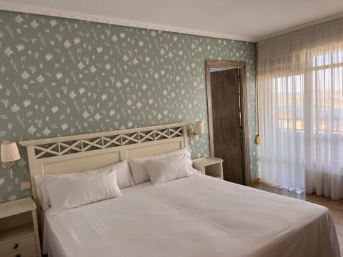 Elegante dormitorio del Hotel Playa de Los Locos en Suances con vistas al mar, cabecero color crema y papel tapiz botánico