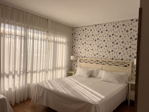Habitación luminosa del Hotel Playa de Los Locos con vistas al mar, ropa de cama blanca, papel pintado floral y cortinas translúcidas en Suances