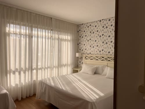Luminosa habitación de hotel en Playa de Los Locos con vistas al mar, ropa de cama blanca, papel pintado estampado y cortinas translúcidas en Suances