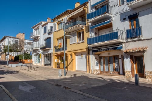 Colorful Mediterranean buildings in Palafrugell city center with yellow and white facades, blue balconies, and street-level