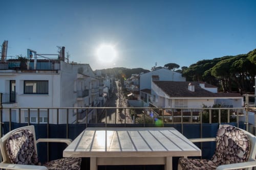 Rooftop terrace overlooking Palafrugell's charming white buildings and pine trees under bright sunlight