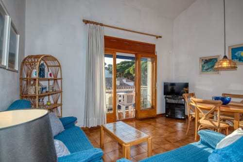 Bright apartment living room in Calella with blue accents, wooden furniture, terrace doors, and sea views in Palafrugell