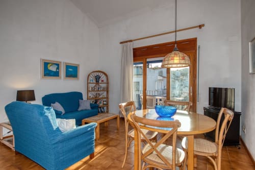 Bright Palafrugell apartment living room with blue furniture, wooden dining table, terrace doors, and city views