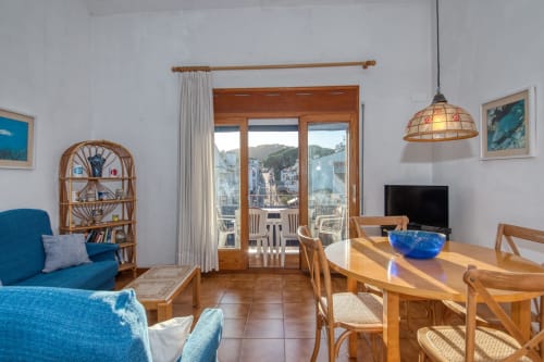 Bright apartment living room in Calella with blue seating, dining table, wooden furniture, and balcony view of the town