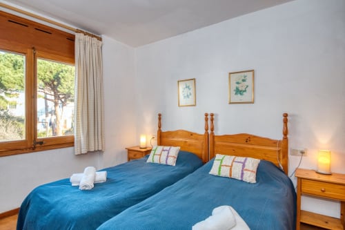 Bright bedroom with twin beds, wooden frames, blue bedding, and city views in Calella apartment