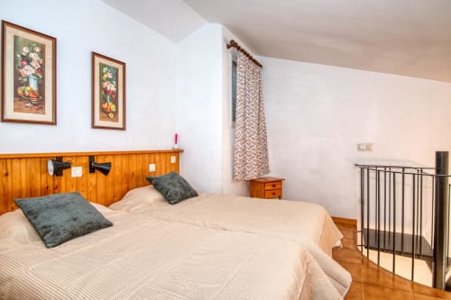 Bright apartment bedroom in Palafrugell with twin beds, wooden headboard, green pillows, and city views from window
